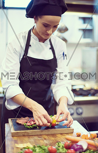 female Chef  in hotel or restaurant kitchen preparing beef steak with vegetable decoration