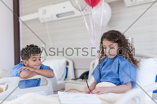 little middle eastern boy and girl painting home and family at hospital bed in a large modern hospital