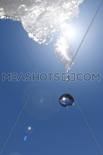 Icicle dripping against blue skies with reflections of the sun in water droplets