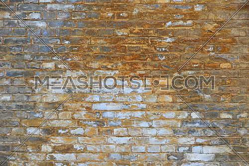 Old grunge vintage yellow and brown painted brick wall with blue and white paint stains and dirt faded background