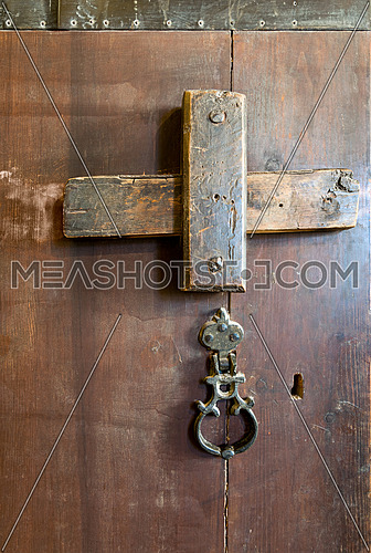 Front view closeup of a wooden aged latch, rusted ring door knob, and keyhole over a wooden opened door