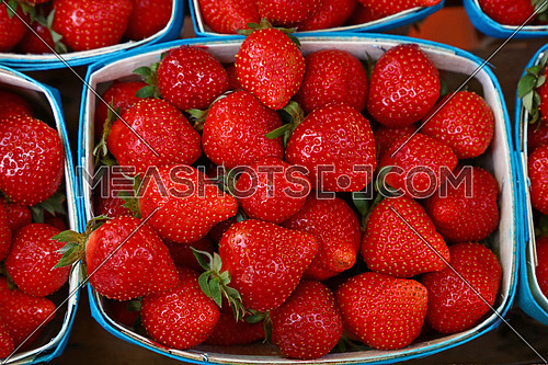 Close up fresh red strawberry berries in wooden container on retail display of farmers market, high angle view