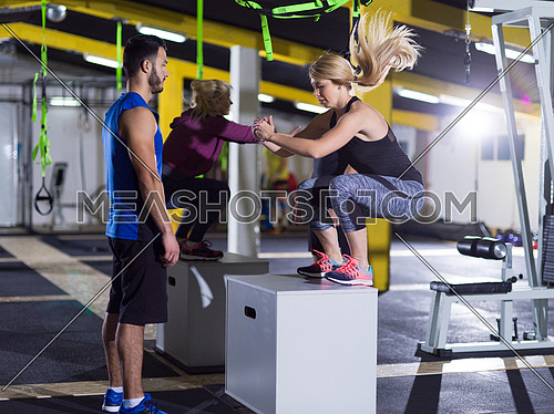 group of young healthy athletic people training jumping on fit box at crossfitness gym