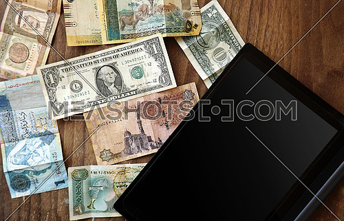 different currencies on wooden background and tablet