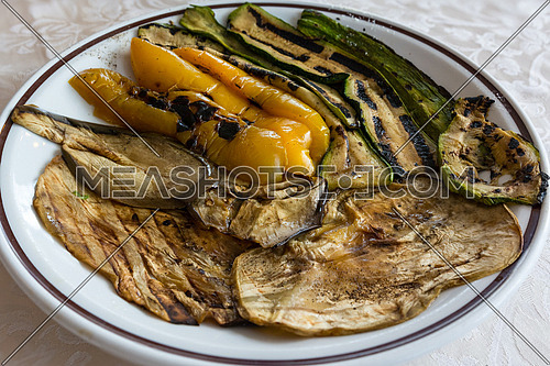 In the picture zucchini, peppers and eggplant grilled and served on white plate at restaurant.