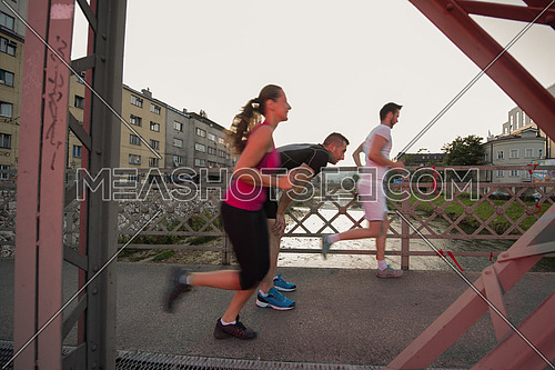group of young sporty people jogging across the bridge at sunny morning in the city