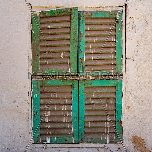 Old grunge window with closed green shutters on dirty bricks stone wall, Cairo, Egypt