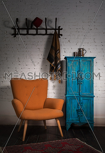 Composition of vintage orange armchair, blue cupboard, wall hanger with ornate scarf and red fez in studio