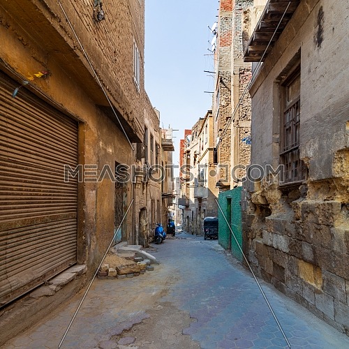 Aged houses with crumbling walls located on narrow abandoned street on sunny day in old Cairo, Egypt
