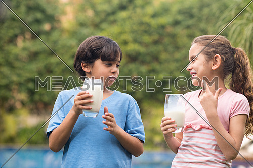 Middle Eastern boy and girl enjoying with a glass of milk in their hands outside on summer day