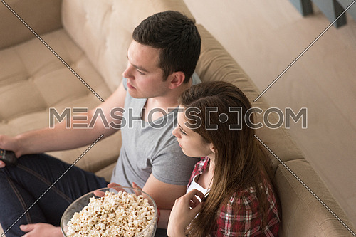 young handsome couple enjoying free time watching television with popcorn in their luxury home villa