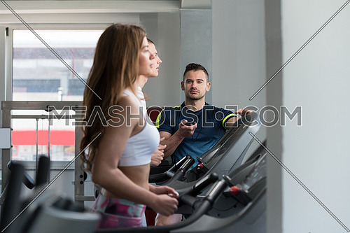 Group Of Young People Running On Treadmills In Gym Or Fitness Club While Personal Trainer Measure Time On Stopwatch