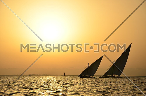 two sail boats in the sea at sunset