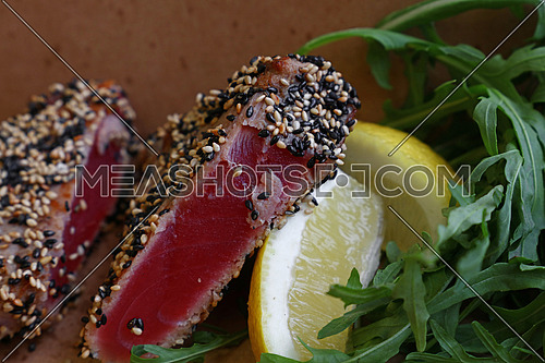Close up street food brown carton box portion of lightly seared tuna steak with sesame seeds and arugula salad
