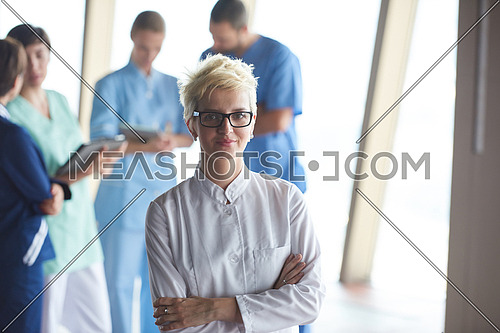 female doctor with glasses and blonde hairstyle  standing in front of team  in background, group of medical staff at hospital