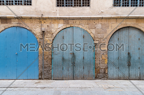 Row of closed three blue weathered wooden arched doors in stone bricks wall, located in old abandoned district