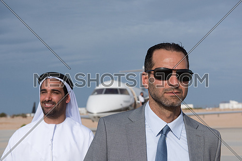 young successful businessman walking with his Arab business partner in front of private airplane