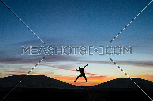 a young man silhouette jumping of joy on a sunset landscape background