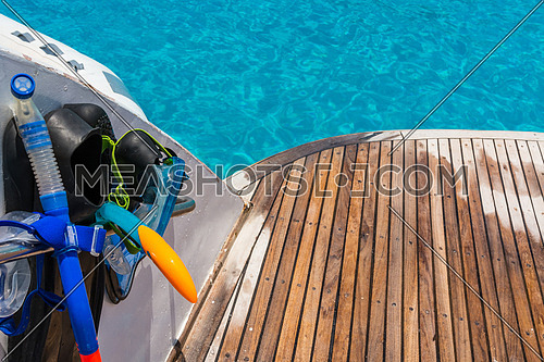 In the pictured boat with curved wooden deck wet,on the left  fins,mask,scuba rubber for snorkeling and in the background ocean blue / turquoise.