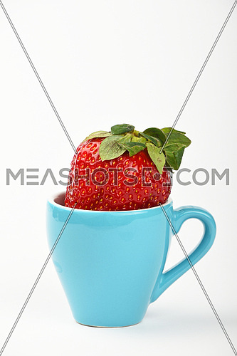 Healthy alternative, one big red ripe mellow strawberry in small blue espresso coffee cup over white background, close up, side view