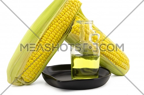 Corn oil in decanter in the cast iron skillet and fresh corncobs next to the cast iron skillet isolated on white background with free copy space for text