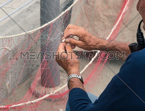 Old fisherman reparing fishing net, sitting with pipe in his mouth.