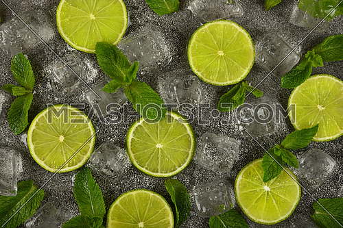 Close up flat lay of lime slices, fresh green mint leaves and ice cubes on grunge gray stone table surface, elevated top view, directly above