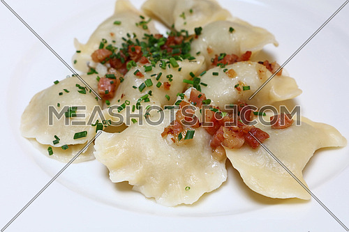 Plate of pierogi or varenyky stuffed filled dumplings with bacon and green chive onion, traditional East Europe cuisine meal popular in Poland, Ukraine, Slovakia, Russia, close up, high angle view
