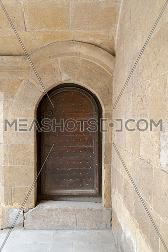 Wooden aged vaulted ornate door and stone wall at caravansary (Wikala) of Bazaraa, Medieval Cairo, Egypt