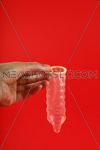 Close up woman hand holding one open latex condom over red background with copy space, low angle side view