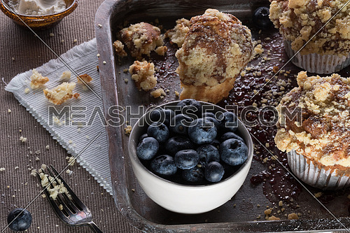 Muffins with crumbs and blueberry in a white bowl on a tray moist with jam and a fork aside