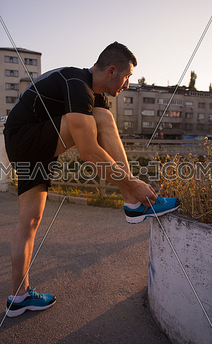 man tying running shoes laces getting ready to run on city at sunny morning