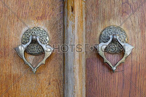 Closeup of two antique copper ornate door knockers over an aged wooden ornate door, Fatih Mosque, Istanbul, Turkey