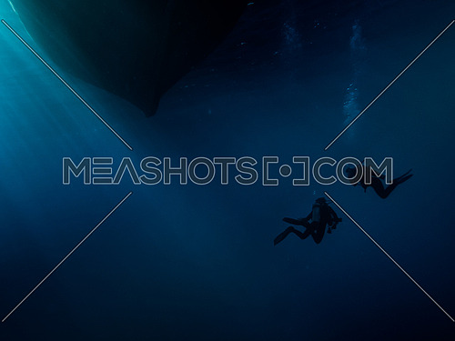 2 scuba divers below  a boat bottom underwater