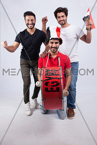 Three young men standing on a white background cheering with a drum for Egypt