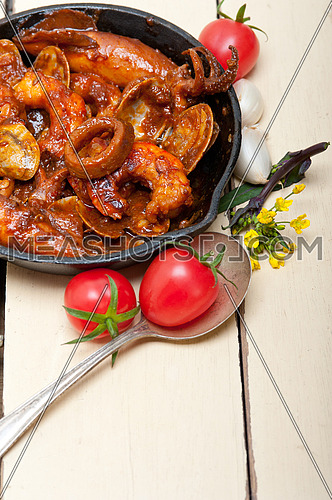 fresh seafood stew prepared on an iron skillet ove white rustic wood table