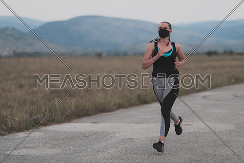 Fitness woman in tight sporty clothes wearing black protective face mask running outdoors in the city during coronavirus outbreak. Covid 19 and physical jogging activity, sport and fitness. New normal