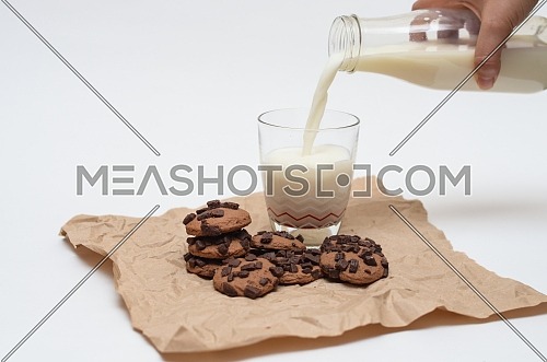 Milk poured from a glass bottle into a glass cup and chocolate chips cookies