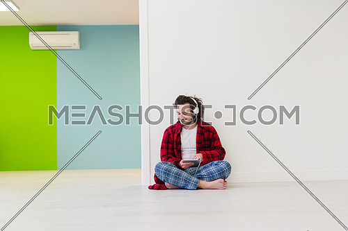 Young handsome man enjoying music through headphones,sitting on the floor at home