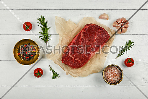 Close up one aged prime marbled raw sirloin beef steak on brown paper parchment wrapping, with spices, over white wooden table background, elevated top view, directly above