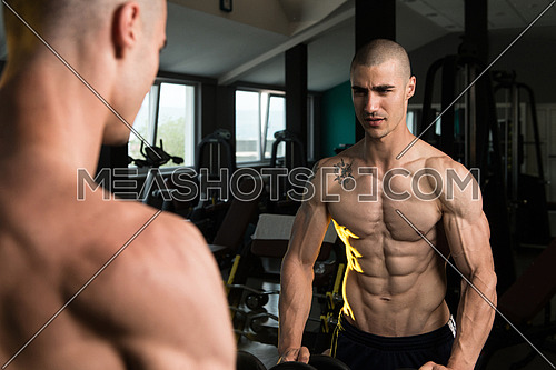 Young Man Standing Strong In Front Of A Mirror And Flexing Muscles - Muscular Athletic Bodybuilder Fitness Model Posing After Exercises