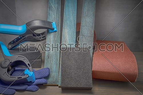 DIY renovation concept still life with safety gloves and small clamps attached to a plank of upright wood in close up