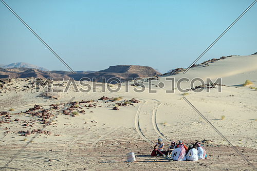 Group of tourists sitting with bedouin guides exploring Sinai Trail from Ain Hodouda at day.