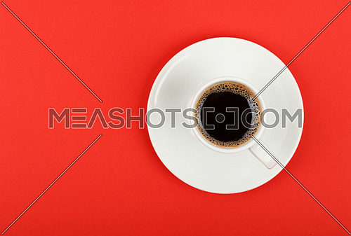 Close up one white cup full of black coffee on saucer over red background, elevated top view, directly above