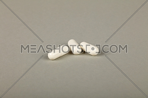 Close up three white gel cap pills of medicine over grey background with copy space, high angle view