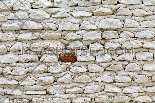 background of old white stone wall with one red brick
