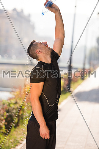 Athlete man runner pouring water from bottle on his head after jogging in the city on a sunny day