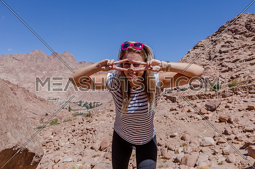 long shot for a female tourist wearing a pink Glasses and travel backpack climbing a big rock to explore Sinai Mountain for wadi Freij by day.