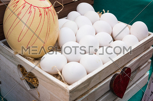 White chicken eggs leaning on straw in wooden basket at market,outdoor.