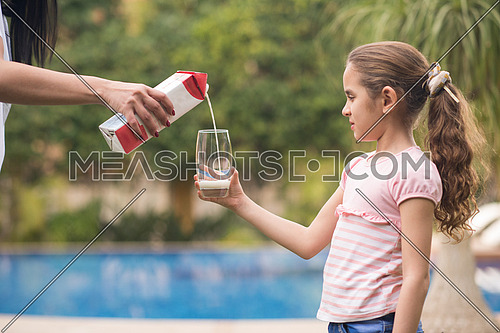 Middle Eastern girl enjoying with a glass of milk in her hand outside on summer day